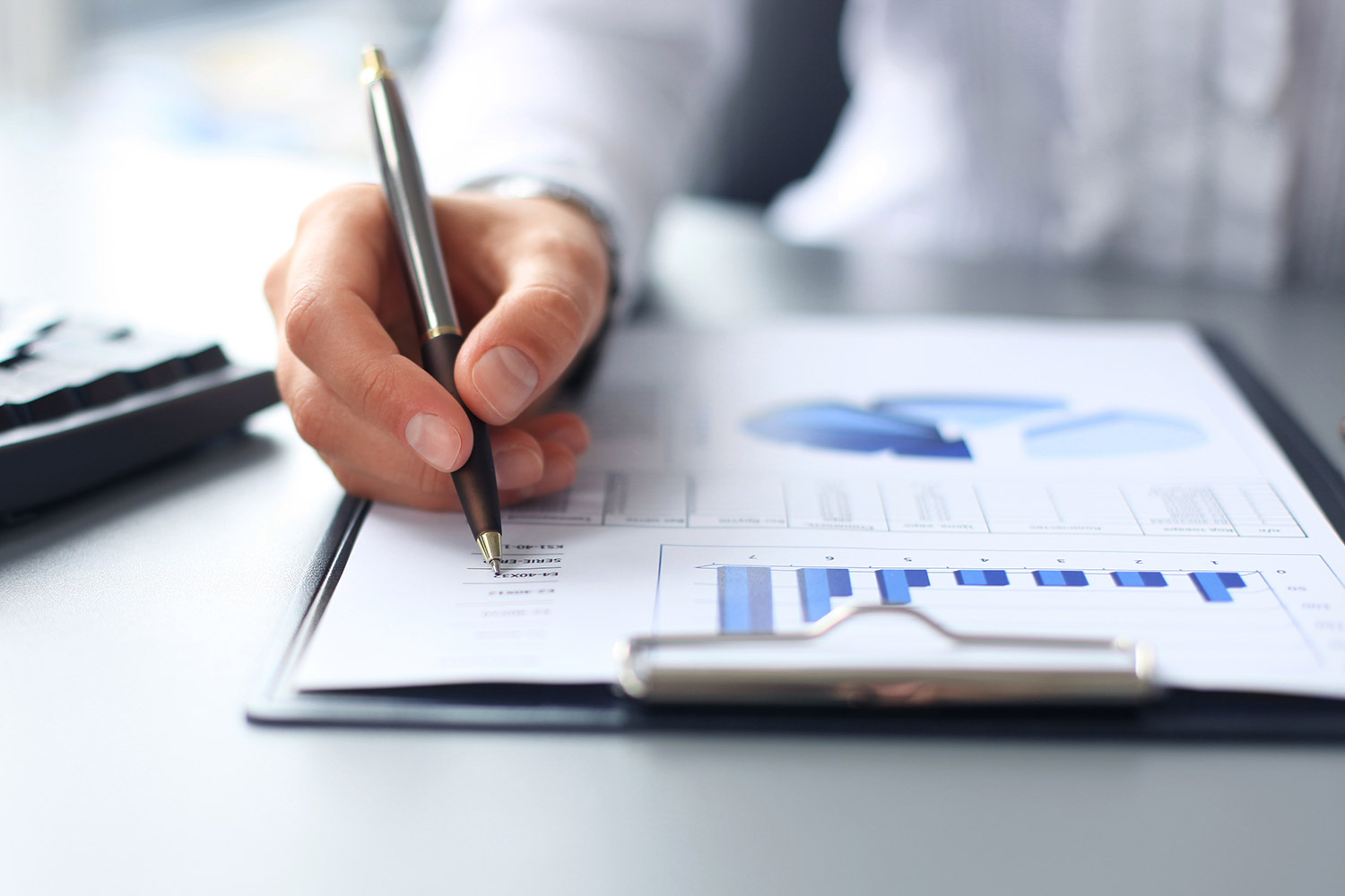 A hand with a pen over a report with charts